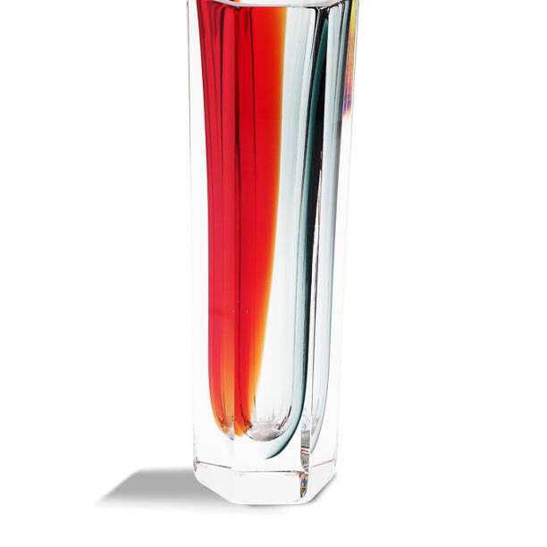 This is an image of a tall, slender glass vase with a vibrant design. The vase features horizontal stripes in red and orange hues that give it a warm appearance, contrasting with the clear base and top. It has a thin neck and mouth, tapering slightly towards the bottom before opening up again to its widest point near the middle. The background is plain and light-colored, which makes the colors of the vase stand out prominently. The lighting in the image highlights the glass's transparency and the reflective quality of the design stripes. There are no visible texts or brands on the vase itself. Keywords: MURANO GLASS, VASE, LAMP MURANO GLASS, DESIGN, MADE IN ITALY, VENICE GLASS