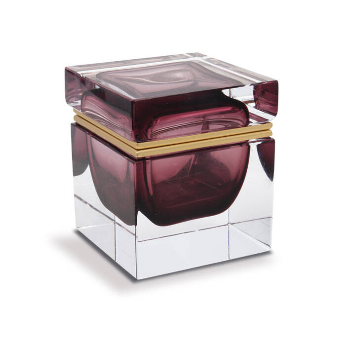 The image shows a beautifully crafted box made of Murano glass. It features intricate designs and patterns characteristic of Venetian glass making, known for their high-quality craftsmanship. The box has a rectangular shape with rounded corners, giving it an elegant and luxurious appearance. The exterior is clear, allowing the viewer to see through to the interior where another layer of red glass adds depth and color contrast to the piece. There are visible seams around the edges, indicating the handcrafted nature of this item. Overall, the box exudes a sense of sophistication and artistry often associated with Murano glass products.