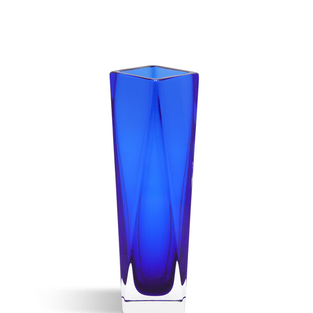 The image shows a tall, slender blue glass vase with a ribbed texture. It's positioned against a neutral background that complements its vibrant color. The design is elegant and modern, with clean lines and a smooth finish. At the bottom of the vase, there appears to be a flat base which provides stability. The light refracts through the glass, creating an interesting play of light and shadow around the base. There are no visible texts or logos in the image that provide additional information about the vase's brand or origin.