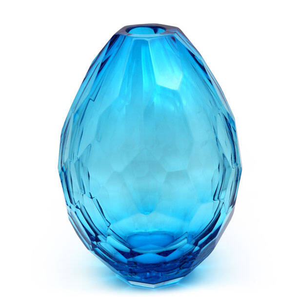 The image shows a blue glass vase with an iridescent sheen, giving it the appearance of sparkling like a gemstone. The shape is rounded and bulbous at the top, tapering slightly towards the base. This type of glassware is often associated with Murano glass, which is a traditional style of glassmaking that originates from the Venetian island of Murano in Italy. The craftsmanship appears to be delicate, suggesting it may have been hand-blown or crafted using techniques specific to Muranese glassmaking, such as lampworking. This particular piece could be used as a decorative item in interior spaces, where its color and reflective quality would catch the light and add visual interest.