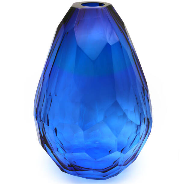 The image shows a beautiful blue Murano glass vase with a distinctive textured pattern. The color gradient is quite noticeable, transitioning from a darker shade at the top to a lighter one towards the bottom. The craftsmanship of this vase suggests it's made by hand, as indicated by the slight irregularities in its shape and the variations in the blue hue. This type of glassware is typically associated with the Murano region in Italy, known for its centuries-old tradition of producing intricate glass art pieces.