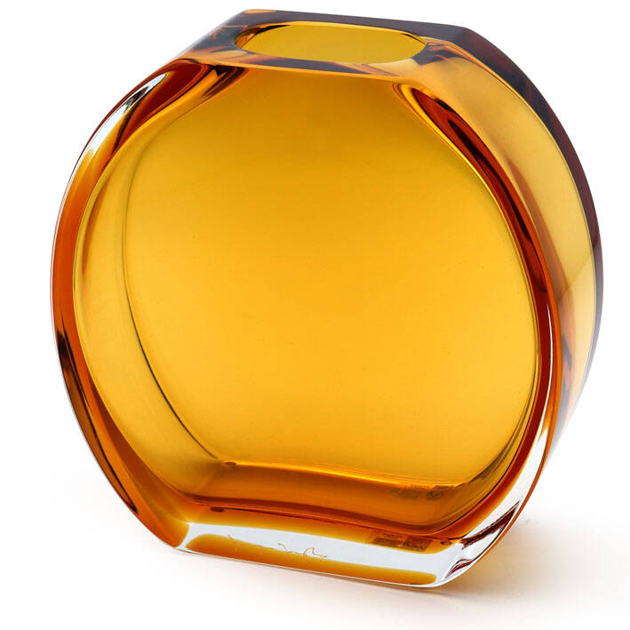 The image shows a piece of Murano glass, which is known for its distinctive design and quality. This particular item appears to be a lamp or possibly a vase with an amber-colored tint, suggesting that it could be designed to hold oil or another type of fluid, although the interior is empty in this photo. The shape is rounded, with a smooth, somewhat irregular exterior that is characteristic of handcrafted glass from Murano. The craftsmanship includes decorative elements and possibly swirls within the glass body, reflecting the artisan's skill in manipulating molten glass to achieve these effects. This item is identified as being made by 