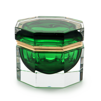 The image shows a piece of Murano glass, which is known for its intricate designs and high-quality craftsmanship. This particular piece appears to be a small vase or decorative container with a green tinted interior. The exterior has a clear base that houses the bulbous body, also featuring a green hue. The top of the piece has a silver or chrome finish, possibly indicating metal accents. The Murano glass is encased within a square-shaped display case made of transparent material, likely designed to protect and showcase the artwork. The name 