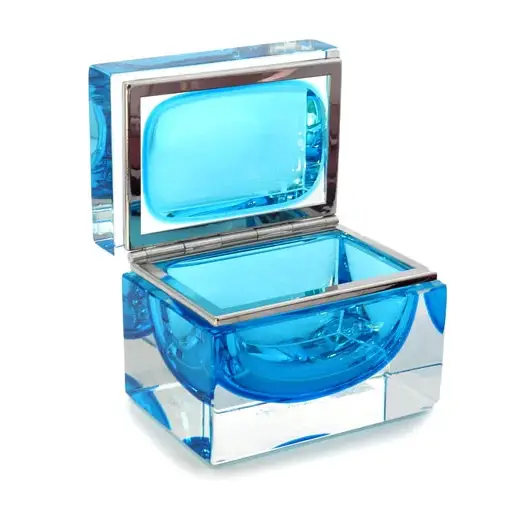 The image shows a small, rectangular glass case with a blue interior. The case is open and features a lid that appears to be hinged, allowing it to stand upright when opened. The interior of the lid is also blue, matching the inside of the case. There's no visible text or branding in the image. This type of container could be used for jewelry, small personal items, or other delicate objects due to its clear and transparent design that allows one to view what it contains without opening the lid. The style of the glass suggests it may be Murano glass, which is known for its intricate designs and made-in-Italy origins, often associated with Venice.