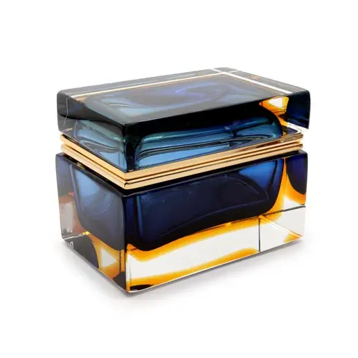 This image showcases a MURANO GLASS box, designed by ALESTANDRO MANDRUZZATO. The glass features a blue and yellow color palette with an intricate pattern that is characteristic of Venetian glassmaking techniques. The design includes swirling patterns, which add a dynamic element to the piece. The box appears to be made up of several individual pieces of glass that fit together, suggesting it's not just decorative but functional as well. The craftsmanship highlights the skill and artistry associated with MURANO GLASS and VENETIAN design. The use of bright colors and detailed patterns indicates a modern twist on traditional Venetian glass art.